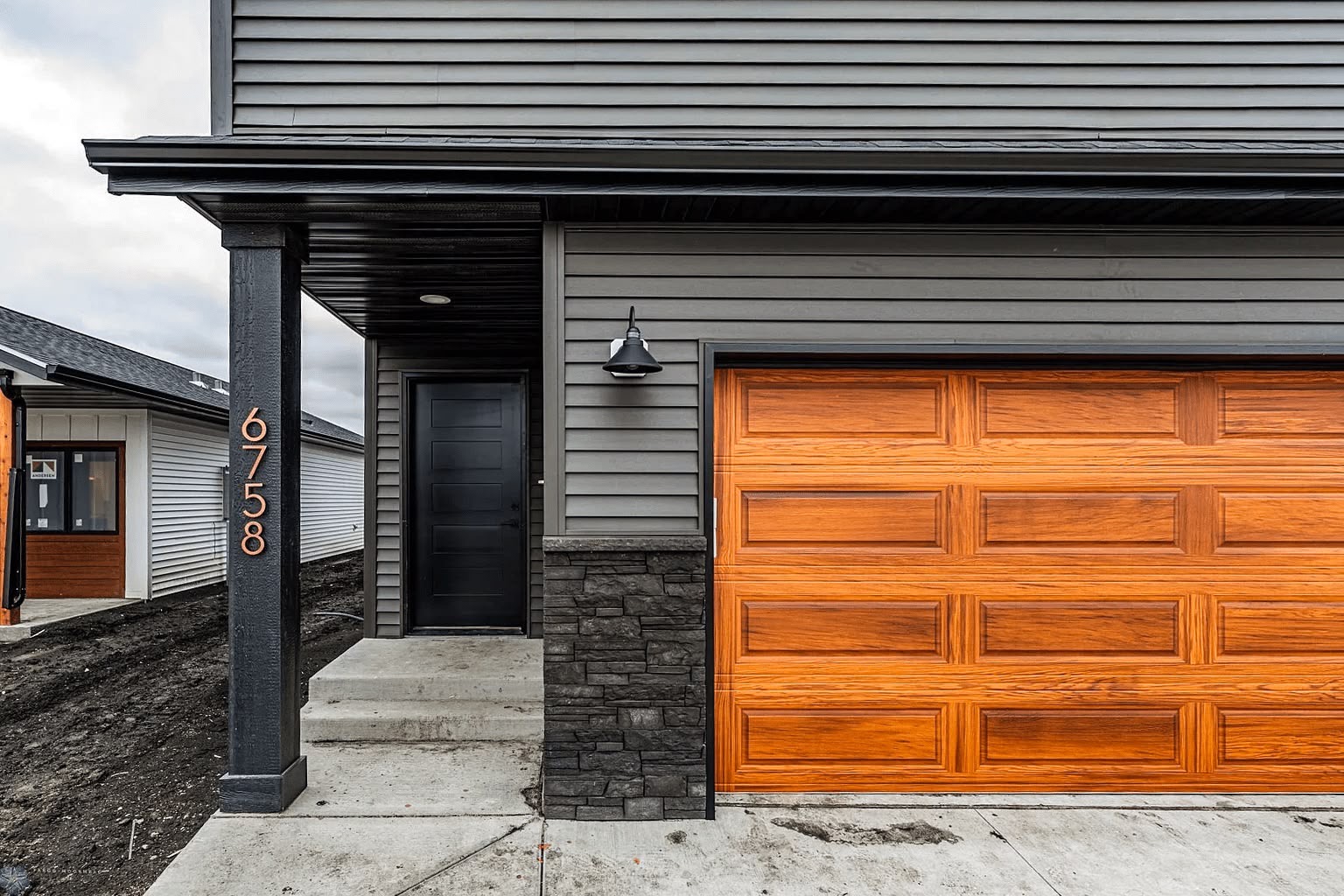 Wood-look raised-panel garage door on a gray-sided home
